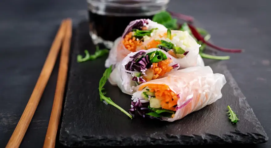 Świeże spring rolls z warzywami i łososiem, podane z sosem.