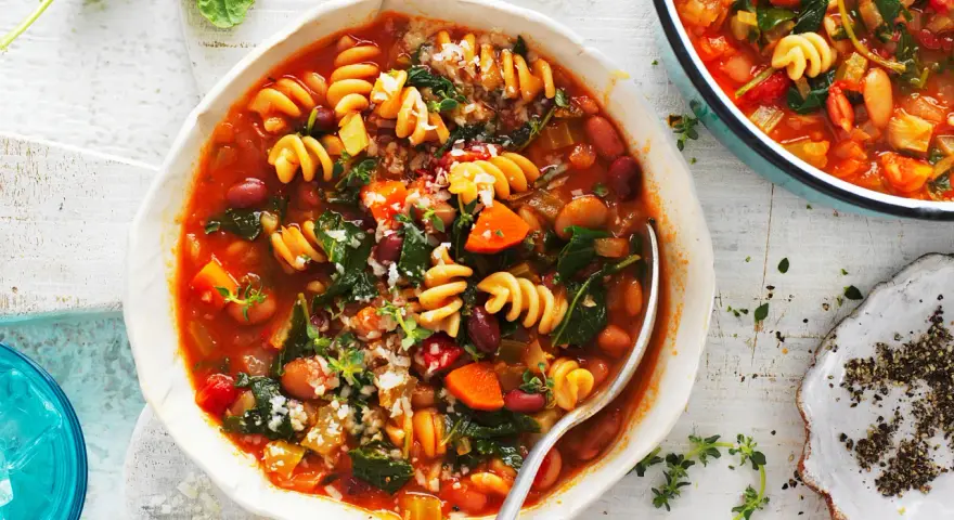 Minestrone co to? Aromatyczna zupa z makaronem, fasolą, warzywami i ziołami, podana w białej misce.