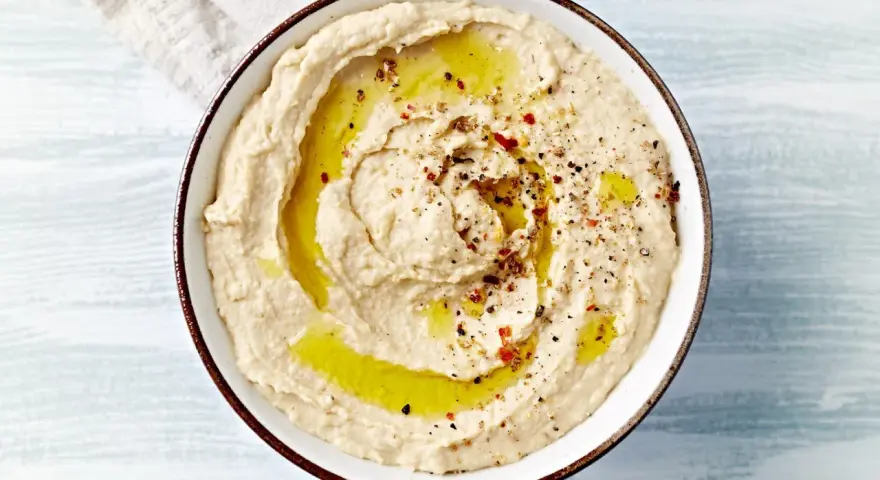 Kremowy hummus polany oliwą, posypany pieprzem i papryką. Idealny do pieczywa, jako dodatek do dań. Prosty hummus przepis.