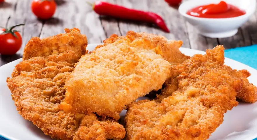 Chrupiące kotlety z kurczaka na talerzu, obok pomidorki i ketchupu. Idealne, gdy zastanawiasz się, ile smażyć kurczaka.