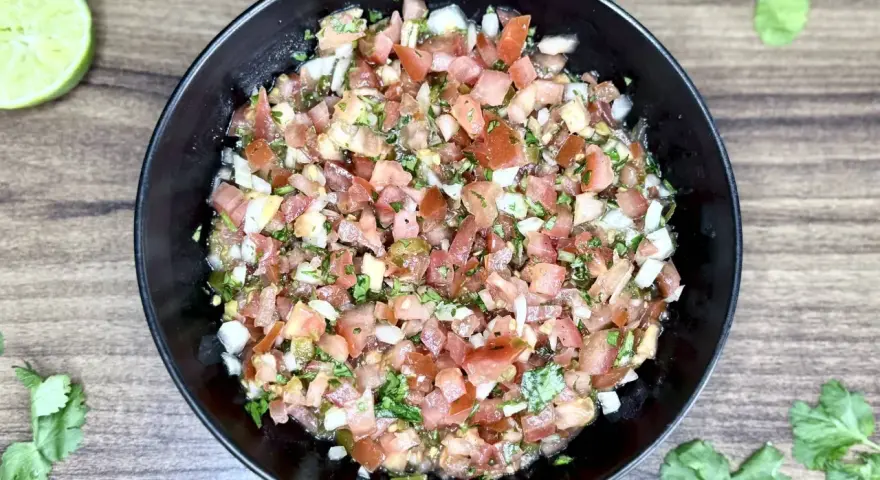 Świeże, posiekane pomidory, cebula, kolendra i papryczka jalapeno tworzą apetyczne pico de gallo w czarnej misce.