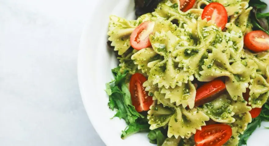 Pyszny makaron z pesto, udekorowany pomidorkami koktajlowymi i świeżą sałatą, podany na białym talerzu.