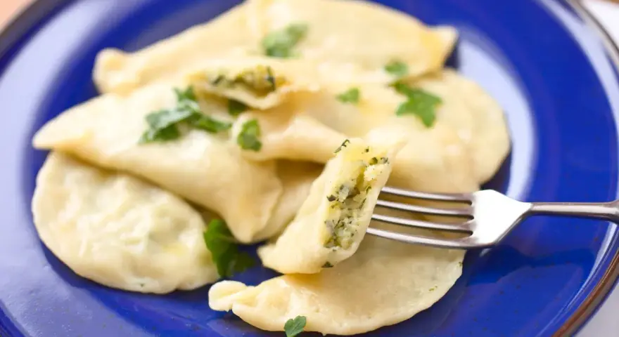 Pyszne pierogi ze szpinakiem i serem, udekorowane natką pietruszki, czekają na widelcu.
