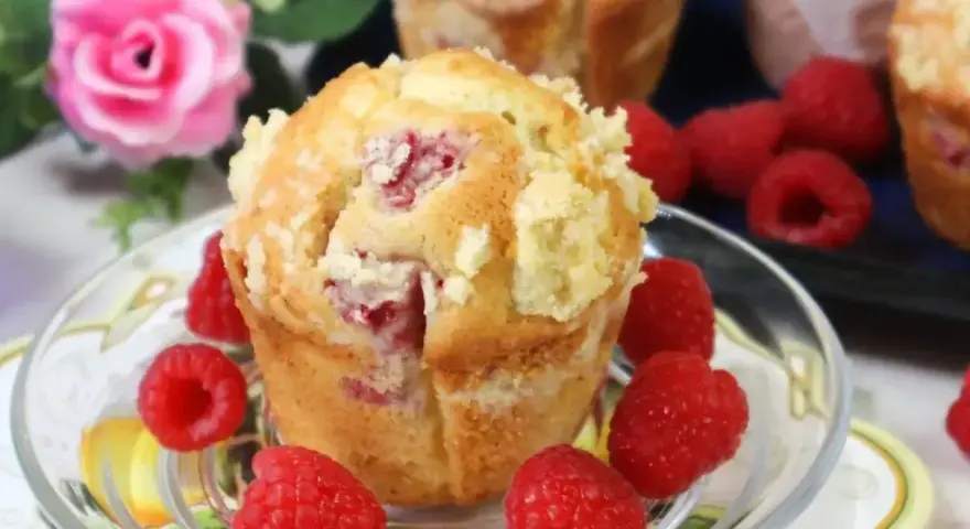 Pyszne muffinki z malinami, posypane kruszonką, otoczone świeżymi malinami. Idealne na deser.