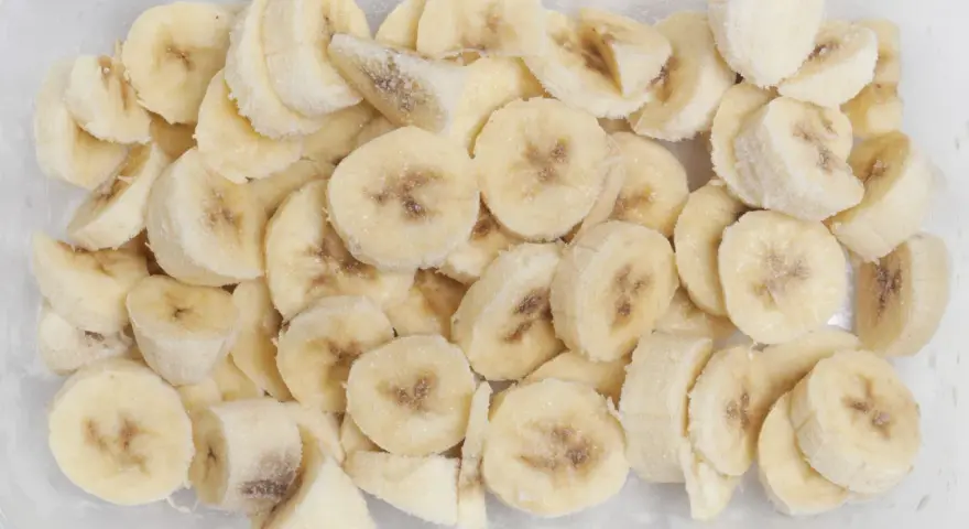 Pokrojone w plasterki banany w pojemniku, pokryte szronem. Tak, banany można mrozić, idealne do smoothie!