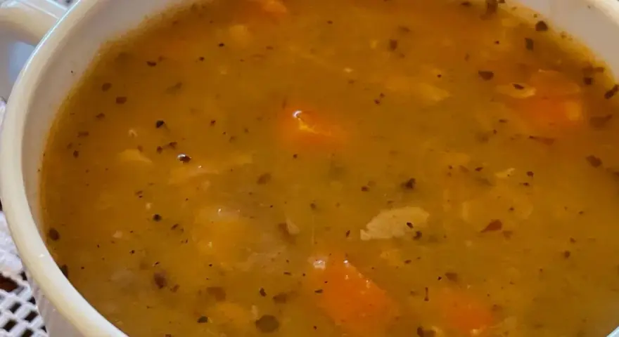 Gęsta, aromatyczna zupa grochowa z kawałkami marchewki i przyprawami, podana w białej miseczce.