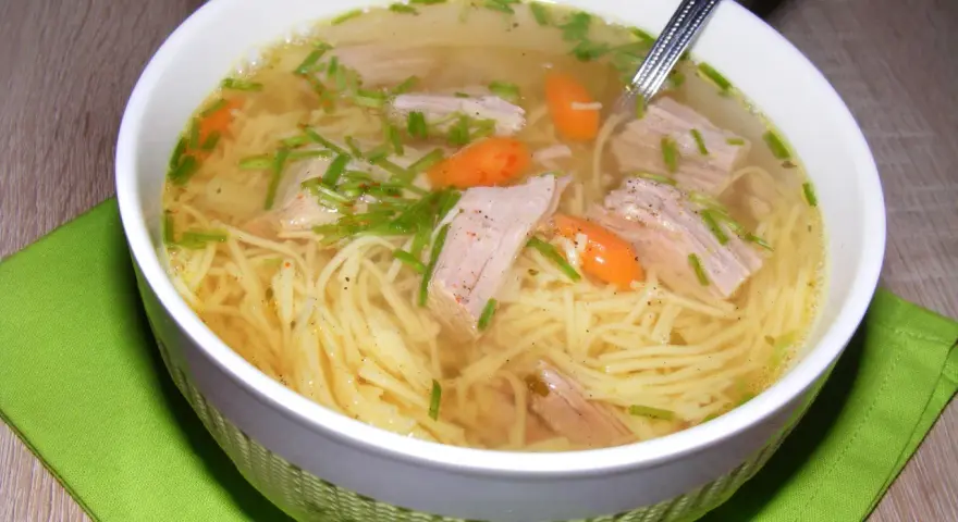 Aromaticzny rosół z indyka z makaronem nitki, kawałkami mięsa i marchewką, posypany szczypiorkiem.