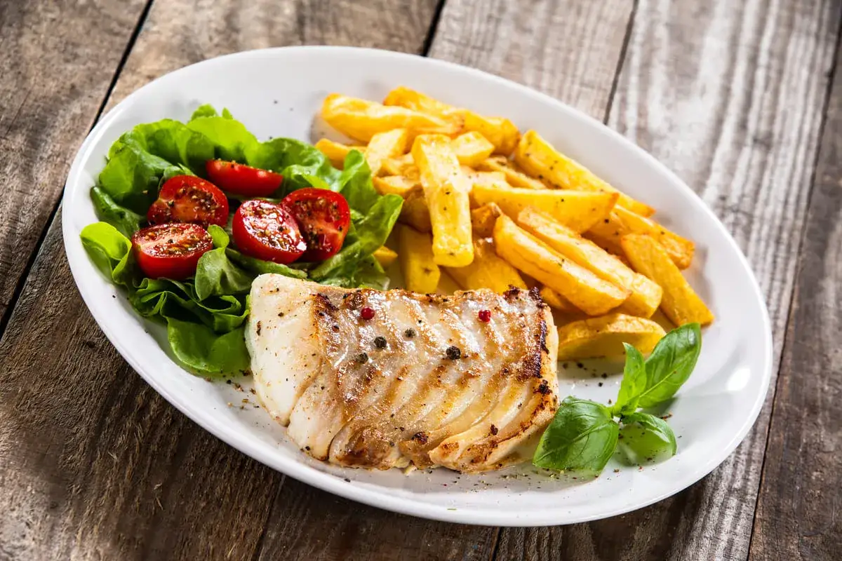 Grillowany filet rybny z frytkami, sałatką i pomidorkami. Idealne przyprawy do łososia podkreślają smak dania.
