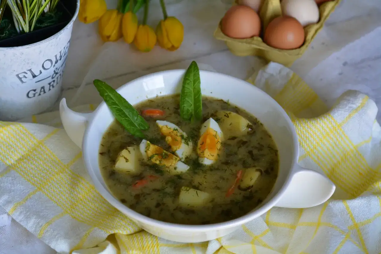 Aromaticzna zupa szczawiowa z ziemniakami i jajkiem, ozdobiona świeżymi liśćmi szczawiu i koperkiem.