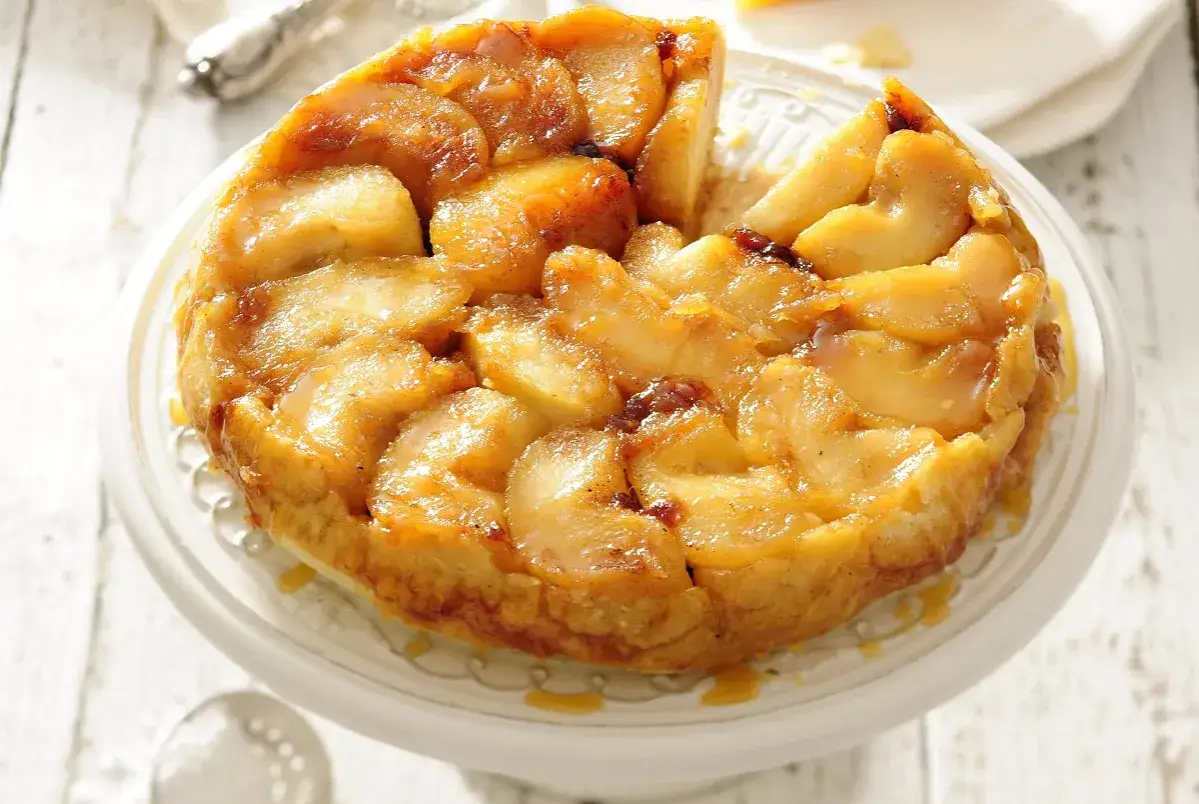 Apetyczna tarta tatin z karmelizowanymi jabłkami, lśniącymi od syropu, na białej paterze.