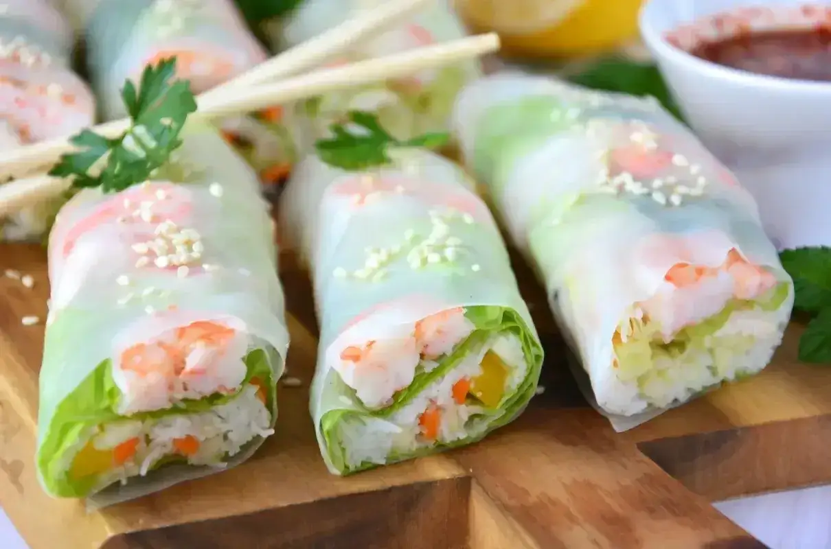 Świeże spring rolls z krewetkami, ryżem i warzywami, posypane sezamem, gotowe do zanurzenia w sosie.