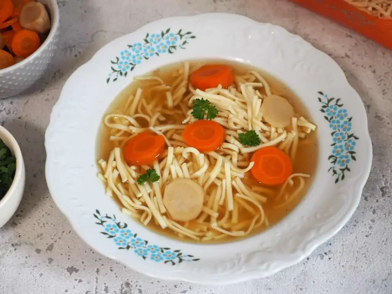 Aksamitny rosół z kaczki z makaronem, marchewką i kawałkami mięsa, ozdobiony natką pietruszki.