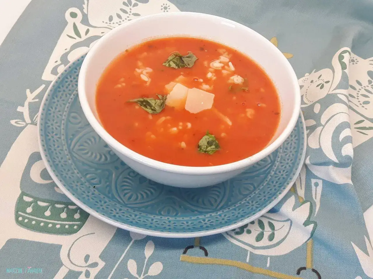 Aromaticzna zupa pomidorowa dla dzieci z ryżem i kawałkami sera, udekorowana listkami bazylii, podana na talerzyku z motywem ptak&oacute;w.