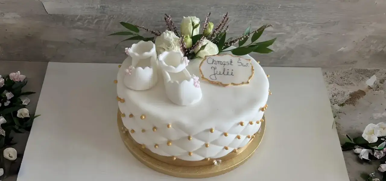 Elegancki, prosty tort na chrzest Julii. Białe buciki, róże i złote zdobienia.