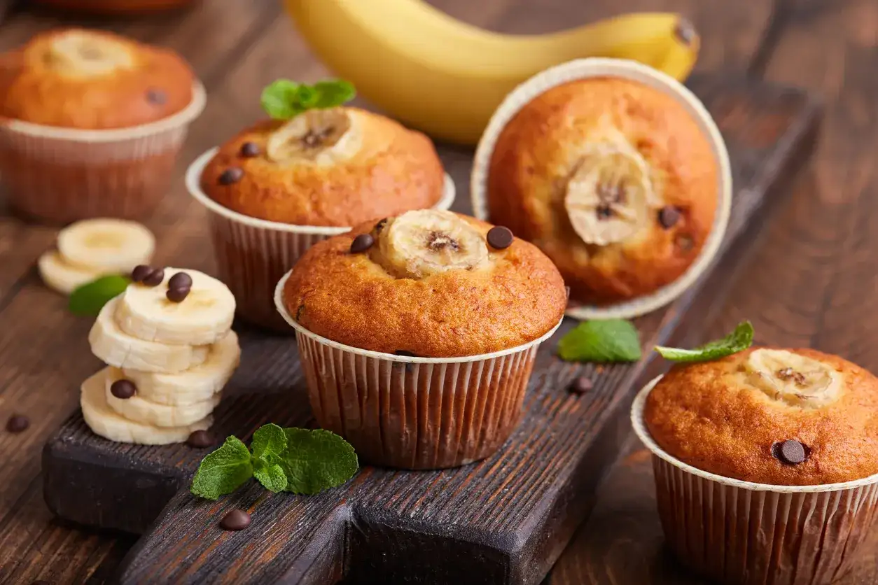Pyszne muffinki bananowe z kawałkami czekolady i plasterkiem banana na wierzchu, udekorowane listkami mięty.