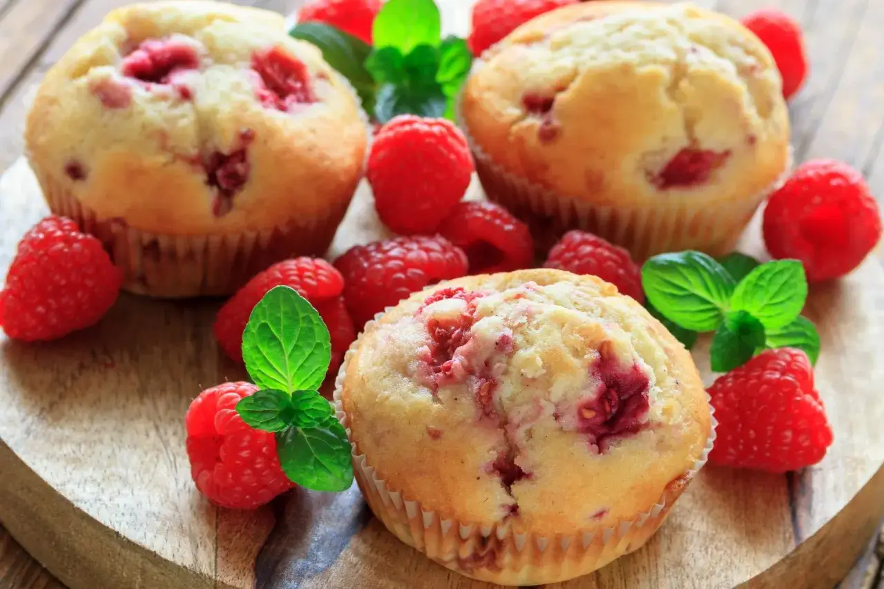 Puszyste muffinki z malinami, ozdobione świeżymi malinami i listkami mięty, kuszą apetycznym wyglądem.