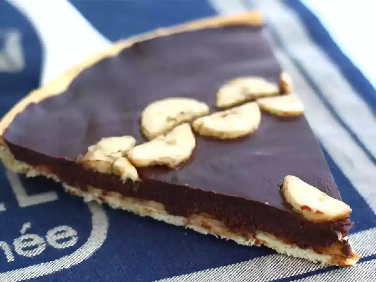 Kawałek pysznej, czekoladowej tarty z bananami, ozdobionej plasterkami owocu.