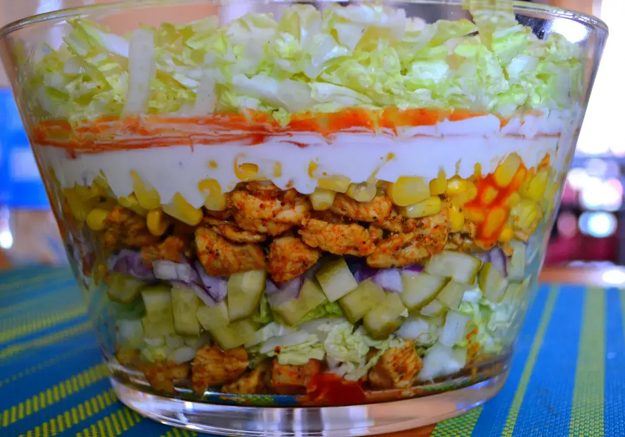 Warstwowa sałatka gyros w szklanej misie: kurczak, kukurydza, og&oacute;rek, cebula, sos.