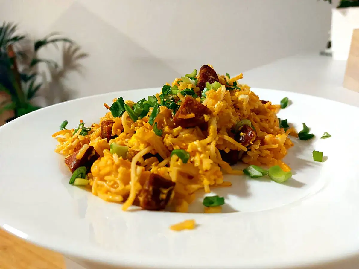Pyszny makaron z chorizo, jajkiem i szczypiorkiem na białym talerzu.