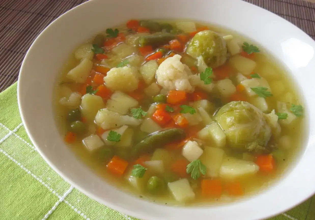 Aromaticzna zupa jarzynowa pełna warzyw: ziemniaków, marchewki, kalafiora, fasolki szparagowej i groszku, udekorowana natką pietruszki.